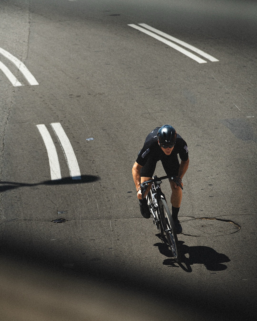 Attaquer rider in black Race kit riding an empty road, shot from above