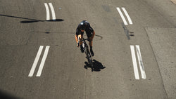 Attaquer rider in black Race kit riding on an empty road marked with white lane lines